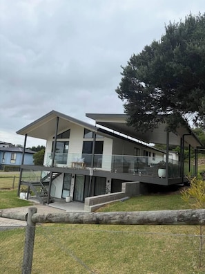 Ein modernes, zweistöckiges Haus mit Balkon, Treppe und einem großen Baum im Hintergrund.