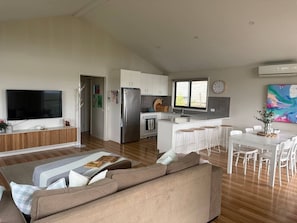 Ein modernes Wohnzimmer mit Fernseher, einer Couch und einem Essbereich mit weißem Tisch und Stühlen.