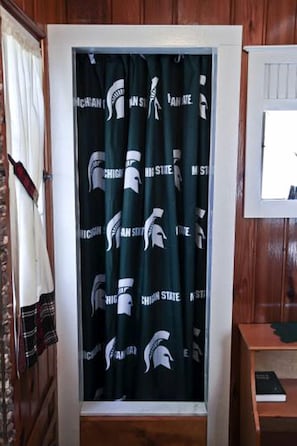Ein Zimmer mit Vorhang, der ein Logo mit spartanischem Helm zeigt, einer Holztür und einem kleinen Holztisch mit einem Buch.