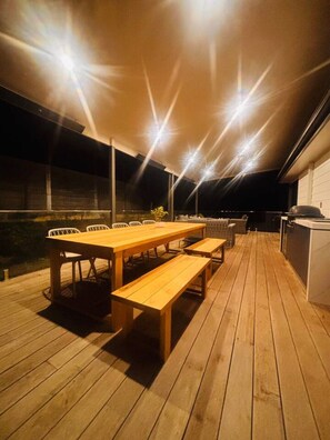 Een terras buiten met een houten tafel en banken, omgeven door een lage muur en een barbecue.
