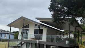 A modern two-story house with a balcony, large windows, and a staircase leading to the upper floor. - Meadow Lees - Linen, Wi-Fi, Pet Friendly (Venus Bay)
