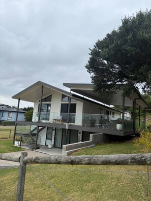 A modern two-story house with a balcony, large windows, and a staircase leading to the upper floor. - Meadow Lees - Linen, Wi-Fi, Pet Friendly (Venus Bay)