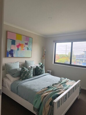 Een slaapkamer met een bed, kussens, een raam en een schilderij.