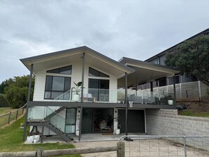 Une maison moderne à deux étages, dotée d’un balcon, de grandes fenêtres et d’un escalier menant à l’étage supérieur.