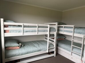 Une chambre avec des lits superposés à trois niveaux, chaque lit étant équipé d’un matelas et d’oreillers.