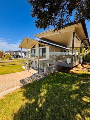 A modern two-story house with a covered patio, a visible staircase, and a well-maintained lawn.