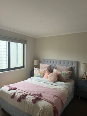 A bedroom with a bed, pillows, a bedside table, a lamp, and a window. - Meadow Lees - Linen, Wi-Fi, Pet Friendly (Venus Bay)
