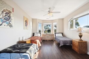A bedroom with two beds, a ceiling fan, a dresser, and a window with a view.