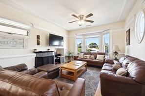Ein Wohnzimmer mit Ledersofas, einem Holztisch, einem Kamin, einem Fernseher und großen Fenstern mit Blick.