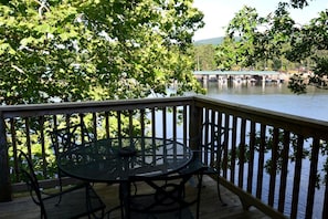 A wooden deck with a round table and chairs, overlooking a calm body of water with a bridge in the background. - Serene Cottage with Pool, Jacuzzi and Lake Views in Mount Ida, Arkansas (Mount Ida)