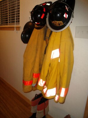 Une paire de vestes jaunes de pompier est accrochée à un mur, avec des bandes réfléchissantes et un casque portant l'inscription « NFDF ».