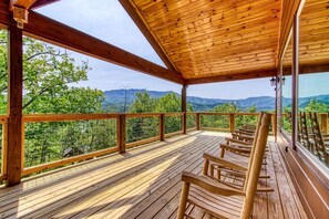 A wooden deck with benches, a glass railing, and a view of mountains. - Secluded Rustic Cottage in Gatlinburg, Tennesee - Ideal Spot for a Family Vacation in the Great Smoky Mountains National Park (Gatlinburg)