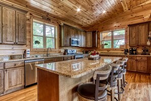 A log cabin kitchen with granite countertops, a central island with bar stools, wooden cabinets, and a large window. - Secluded Rustic Cottage in Gatlinburg, Tennesee - Ideal Spot for a Family Vacation in the Great Smoky Mountains National Park (Gatlinburg)