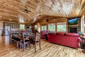 A spacious cabin interior with a dining area, a red sofa, a fireplace, and a stone wall. - Secluded Rustic Cottage in Gatlinburg, Tennesee - Ideal Spot for a Family Vacation in the Great Smoky Mountains National Park (Gatlinburg)