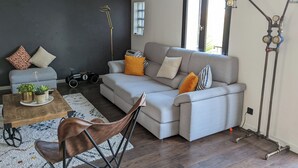 Un salon moderne avec un canapé gris, une table basse en bois, un fauteuil en cuir marron, une maquette de voiture ancienne et une lampe au style industriel unique.