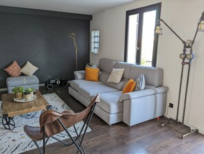 Ein modernes Wohnzimmer mit einem grauen Sofa, einem Holztisch, einem braunen Ledersessel, einem Modell eines Oldtimers und einer einzigartigen industriellen Lampe.