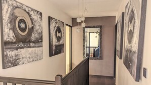 Un couloir orné d’œuvres d’art, un escalier et une vue sur une autre pièce.