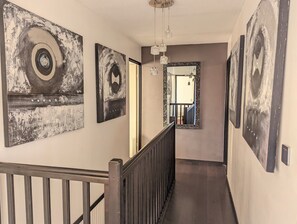Ein Flur mit Kunstwerken an den Wänden, einer Treppe und Blick in einen anderen Raum.