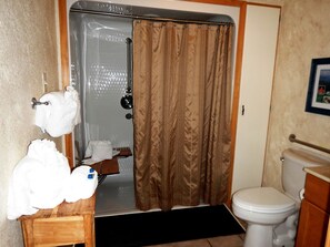 Ein Badezimmer mit Duschvorhang, Toilette und einem hölzernen Hocker mit Handtüchern.