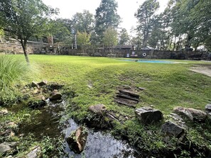 Eine grüne Wiese mit einem kleinen Bach, Felsen und einem Teich im Hintergrund.