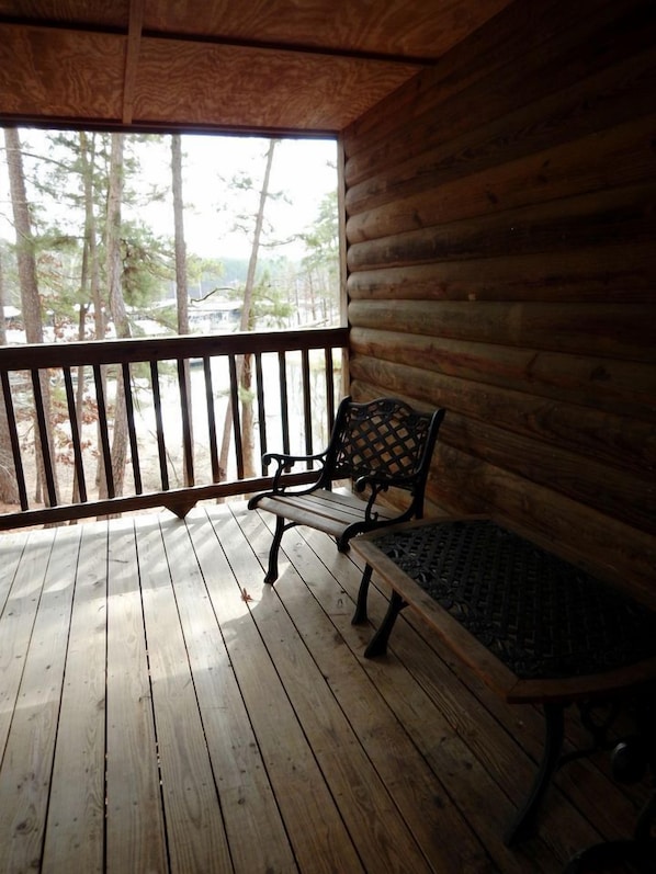 A wooden deck with a bench and railing, overlooking a forested area.