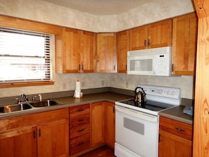 A compact kitchen with wooden cabinets, a microwave, a stove, and a sink.