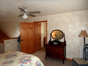 A bedroom with a bed, a dresser, a mirror, a ceiling fan, and wooden doors.