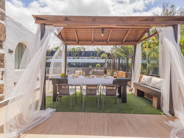 Eine Terrasse im Freien mit einer Holz-Pergola, einem Essplatz und einer Steinwand im Hintergrund.