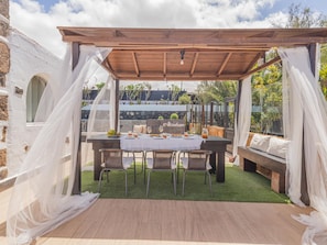 An outdoor patio with a wooden pergola, a table set for dining, and a stone wall in the background. - CHL Villa Abraham Grupos Piscina Privada (Puerto del Rosario)