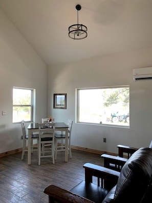 A dining area with a table and chairs, a hanging light fixture, and large windows with a view of the outside. - Charming, Glamping Cabin with Barbecue Grill, Perfect for Wildlife Watching in Raton, New Mexico (Raton)