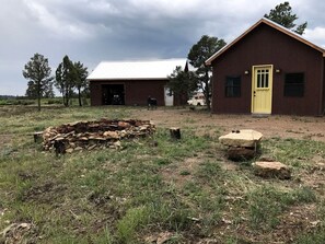 A rustic building with a yellow door, a stack of firewood, and a pile of logs in a grassy field. - Charming, Glamping Cabin with Barbecue Grill, Perfect for Wildlife Watching in Raton, New Mexico (Raton)