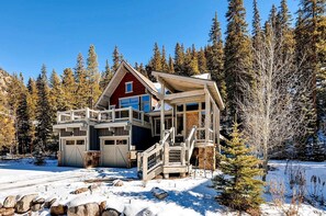 A cabin with a red front, a balcony, and a stone foundation.
