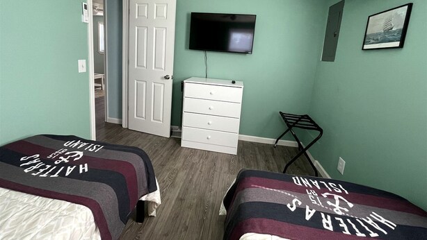 Een slaapkamer met twee bedden, een televisie, een dressoir en een deur naar een andere kamer.