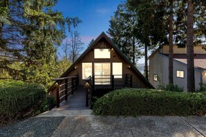 A cabin with a wooden exterior, a staircase leading to a deck, and a view of the surrounding forest.