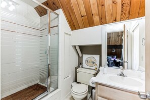 A bathroom with a glass shower enclosure, a toilet, a sink, and a mirror. - Charming A-Frame with Stunning Views in Kelseyville, California (Kelseyville)