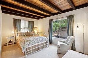A bedroom with a bed, a chair, a nightstand, a lamp, and a window with curtains. - Charming A-Frame with Stunning Views in Kelseyville, California (Kelseyville)