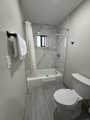 A bathroom with a bathtub, toilet, and a shower area.