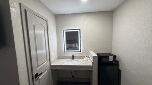 Un baño pequeño con lavamanos, espejo y un refrigerador negro.