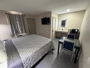 A bedroom with a bed, a desk, a chair, a television, a mirror, and a bathroom with a sink and a toilet.