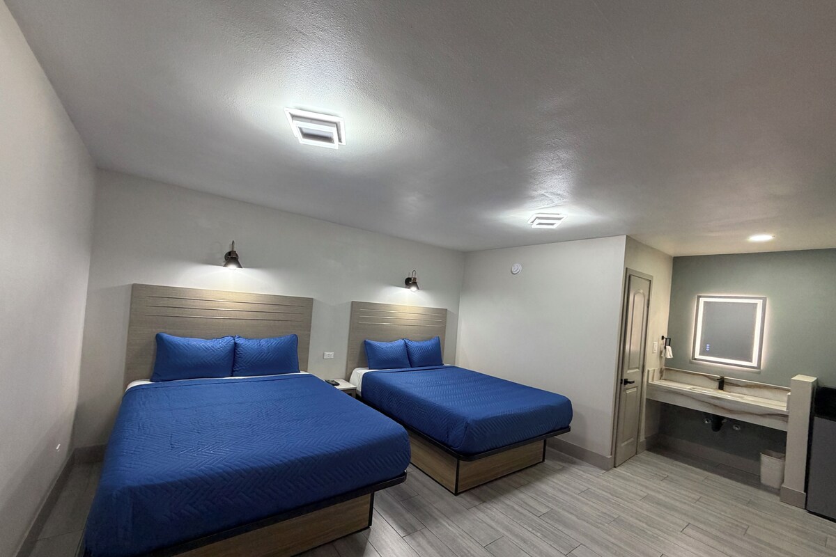 A hotel room with two beds, a bathroom with a mirror, and a small desk.