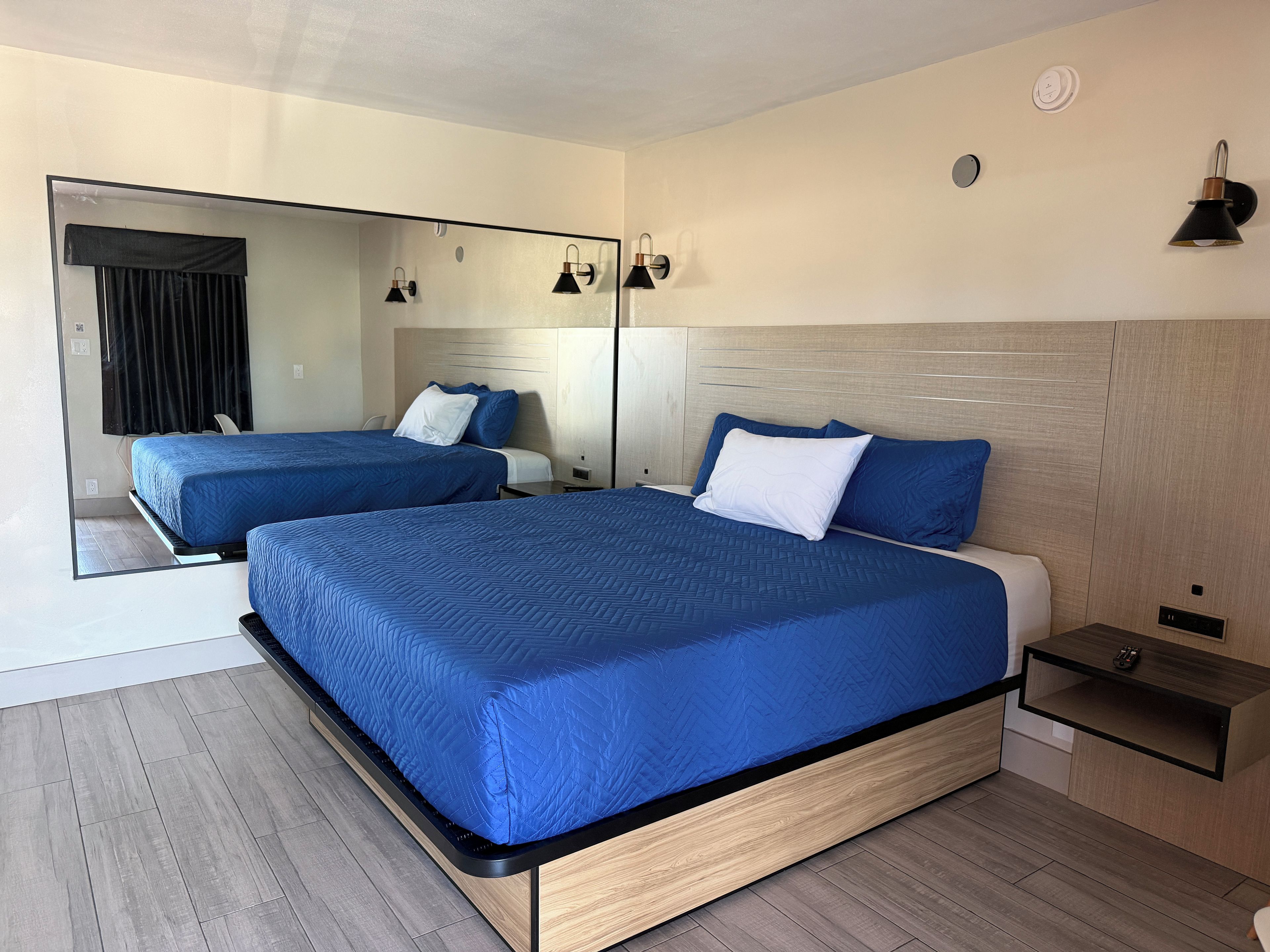 Une chambre d’hôtel moderne avec deux lits, un grand miroir et une table de chevet équipée d’une télécommande.