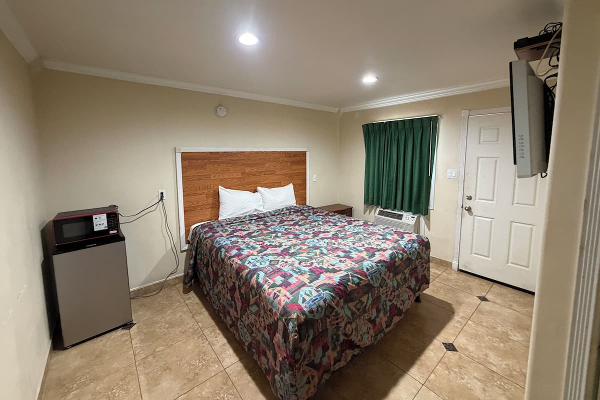A hotel room with a bed, a small kitchenette, a television, and a window with curtains.