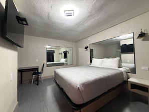 A hotel room with a large bed, a flat-screen TV mounted on the wall, a bedside table, and a mirror.