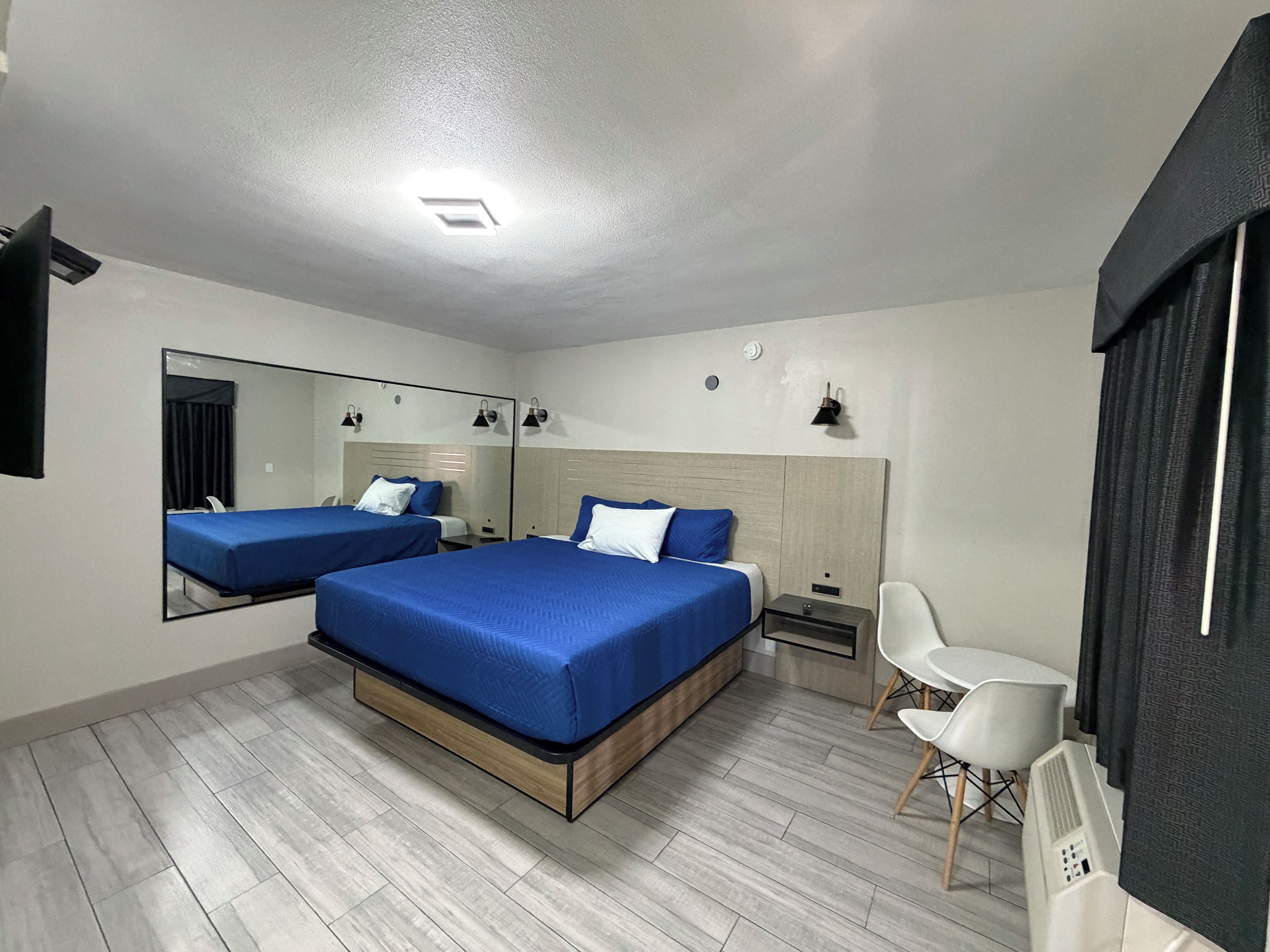 Une chambre d’hôtel moderne équipée de deux lits, d’un grand miroir, d’une table de chevet, d’une chaise et d’un téléviseur à écran plat.