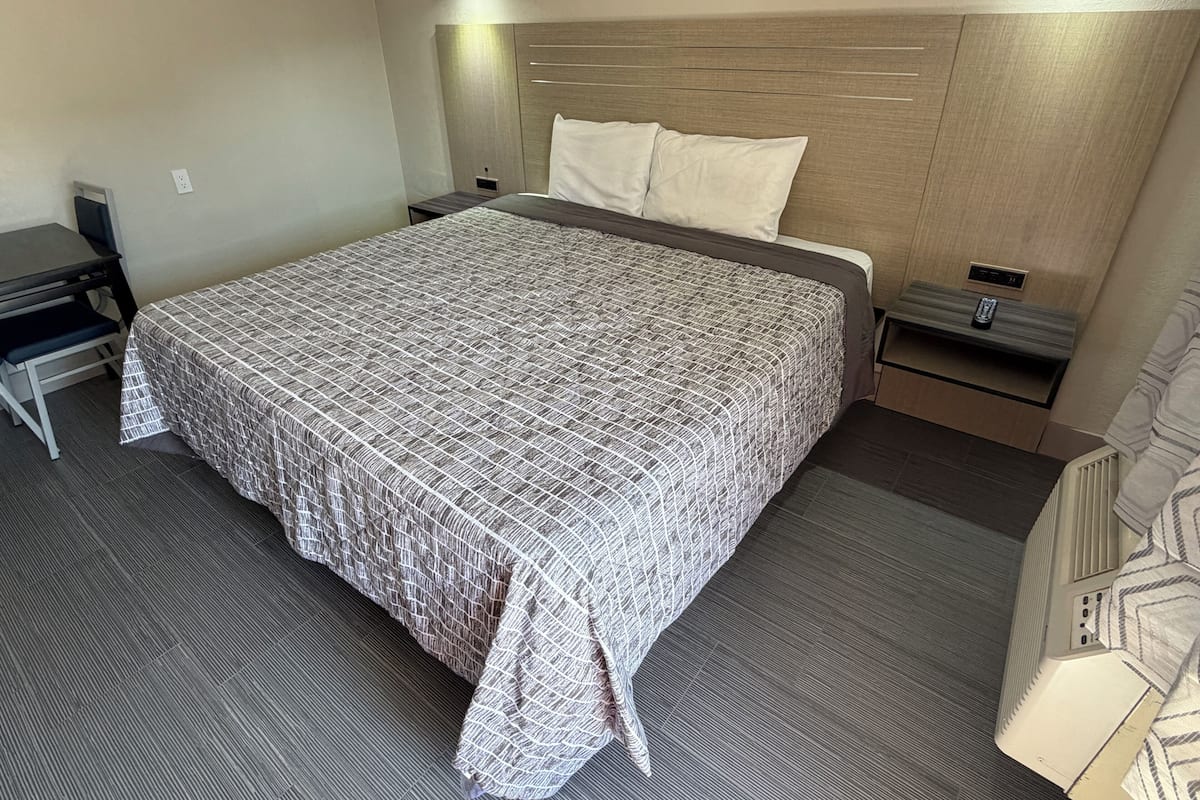 A neatly arranged hotel room with a large bed, a desk, a chair, a bedside table, and a wall-mounted lamp.