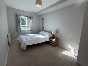Ein Schlafzimmer mit einem Bett, einem Nachttisch mit Lampe, einem Fenster mit Vorhängen und einer Heizung.