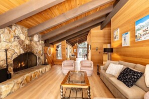 A cozy living room with a stone fireplace, wooden beams, a glass coffee table, and a sofa with a patterned pillow. - Spectacular Cabin with Foosball and Fireplace in Truckee, California (Truckee)