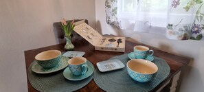 A table with four cups and saucers, a small vase with flowers, and a box with a coffee-making set.