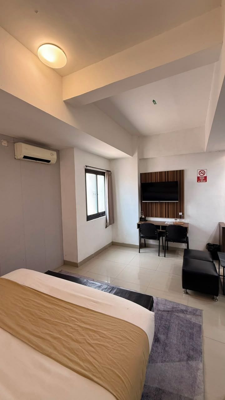 A hotel room with a bed, a desk, a television, and an air conditioning unit.