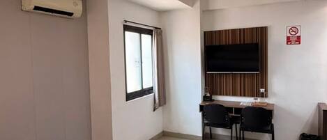 A hotel room with a bed, a desk, a television, and an air conditioning unit.